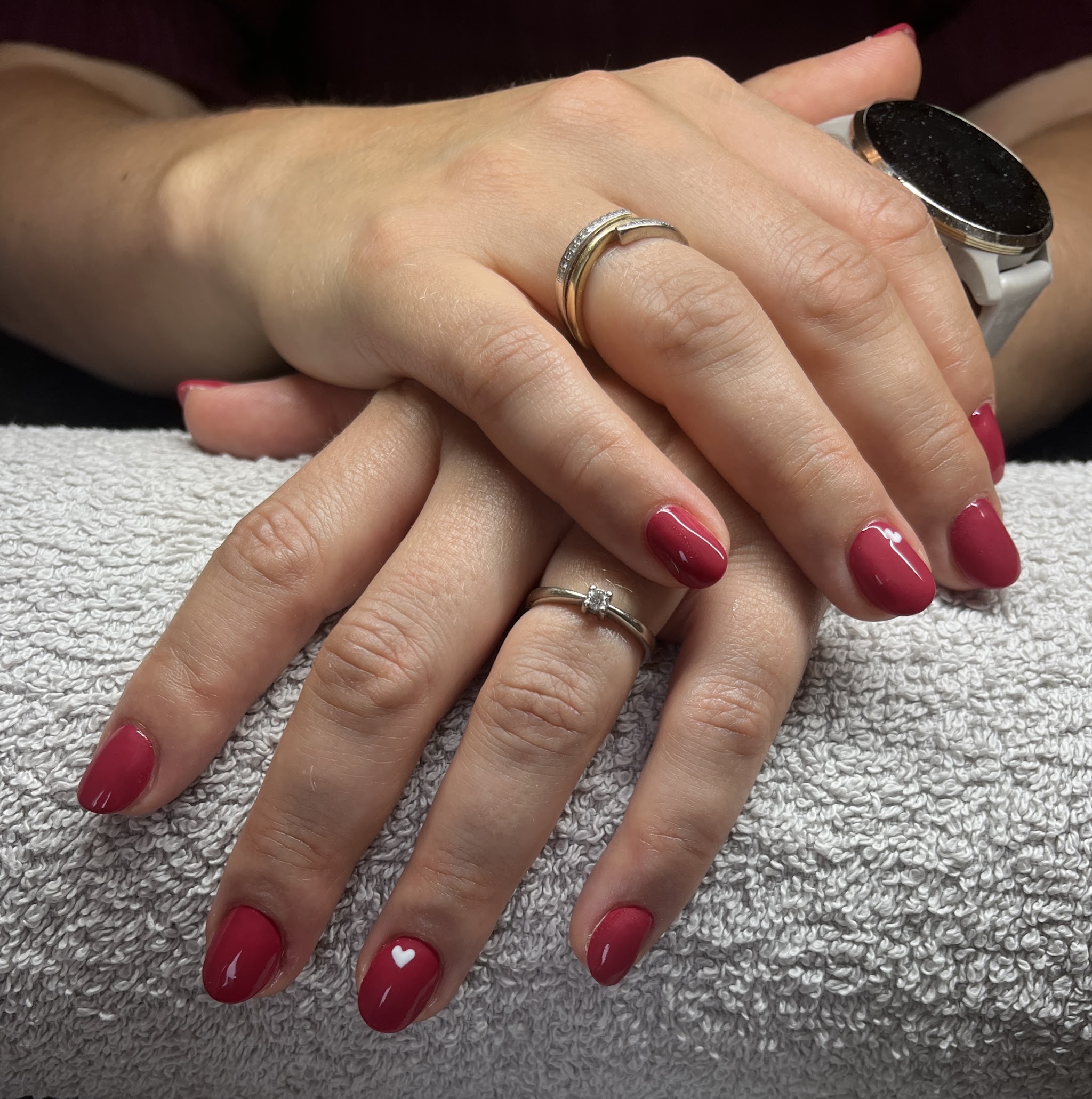 Handen op een grijze handdoek met korte, ronde nagels in framboosrood