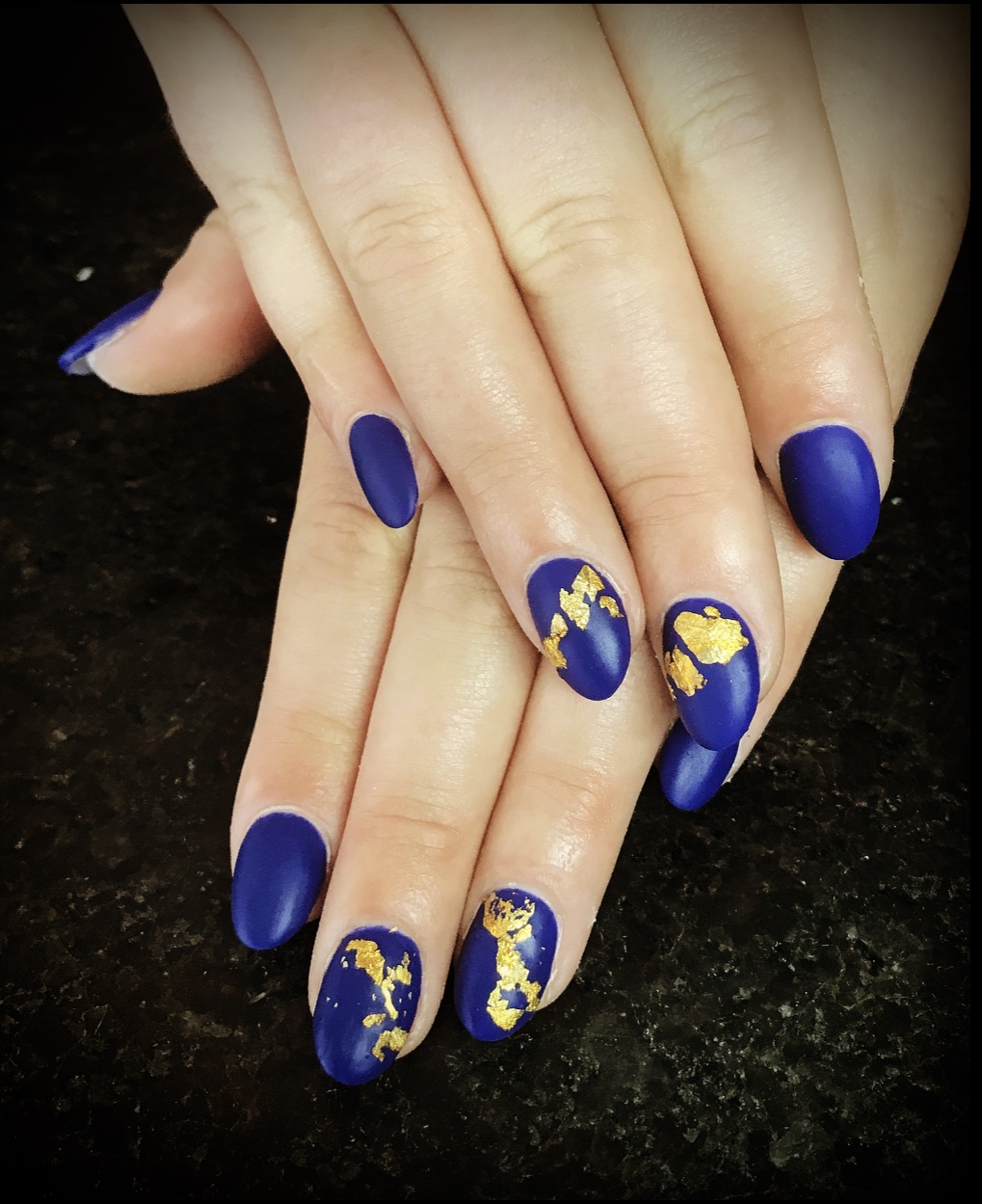 Amandelvormige nagels in matblauw met bladgoud, op een donkere achtergrond