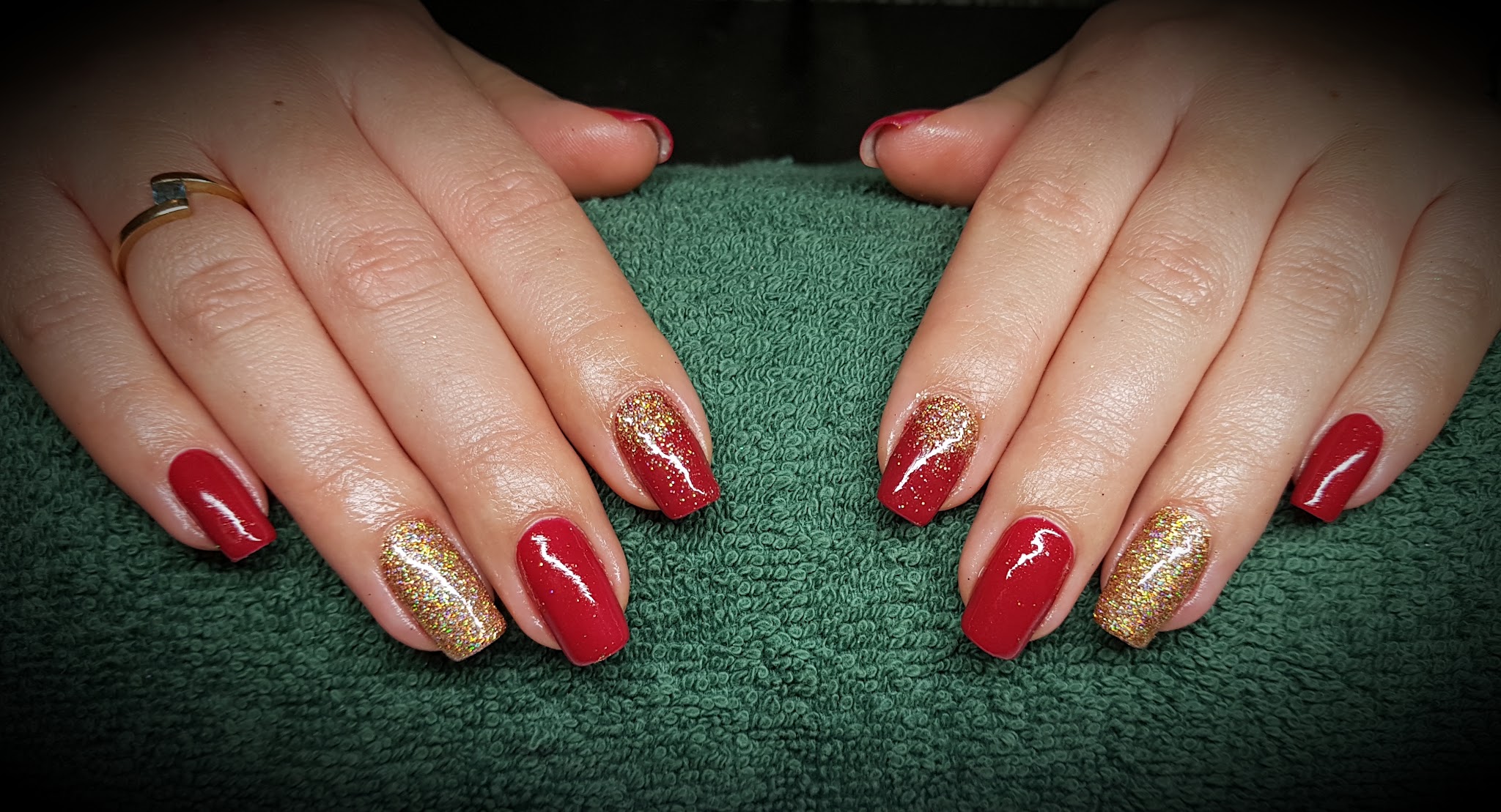 Handen op een groene handdoek met glanzend rode nagels en gouden glitter op de ringvingers