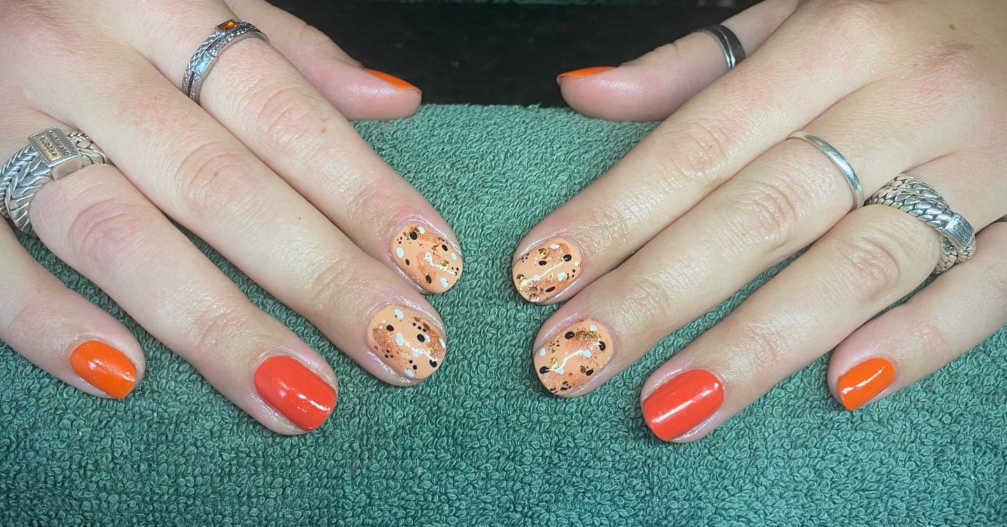 Handen op een groene handdoek met nagels in tinten oranje, en spikkels op nude op twee nagels per hand