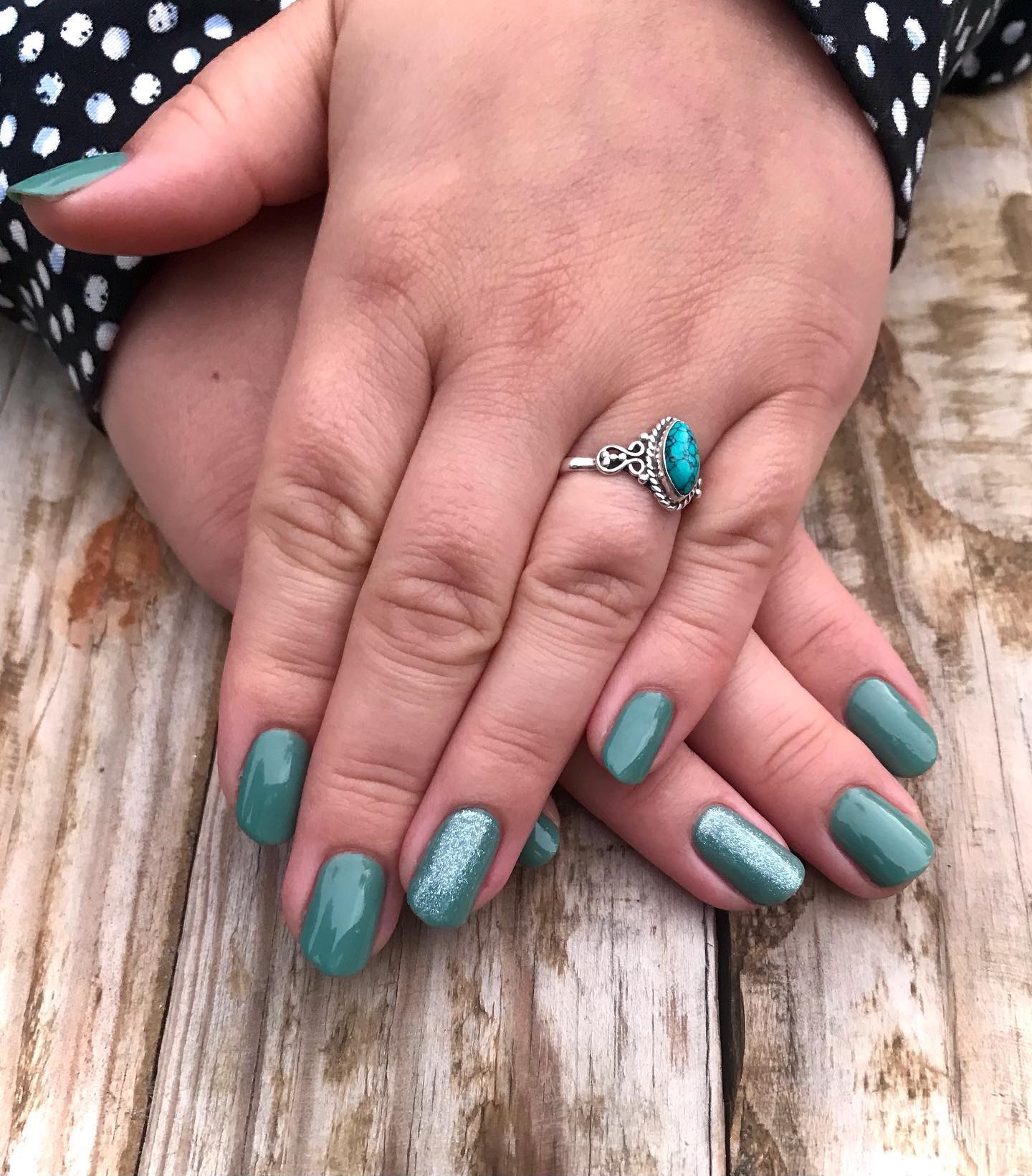 Handen op een houten tafel met turquoise glitternagels en een zilveren ring met turquoise steen